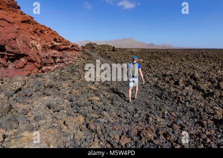 A man with a backpack trekking along a rocky route in volcanic landscape of Timanfaya National Park on Lanzarote, the Canary Islands, Spain Stock Photo