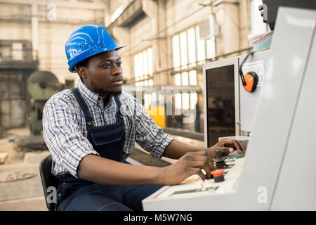 Portrait shot of highly professional worker wearing checked shirt and overall operating machine at production department of modern plant Stock Photo