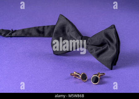 Black bow tie with cufflinks on purple background. Stock Photo