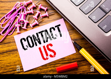 Handwritten text showing Contact Us. Business concept for Customer Support written on pink sticky note paper on wooden background next to keyboard. Wi Stock Photo