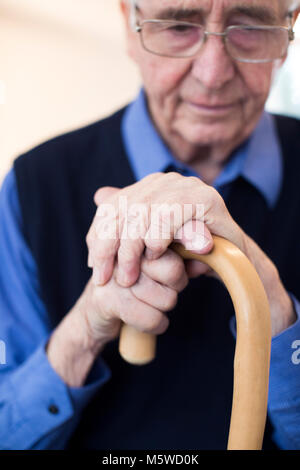 Sad Senior Man Sitting In Chair Holding Walking Cane Stock Photo