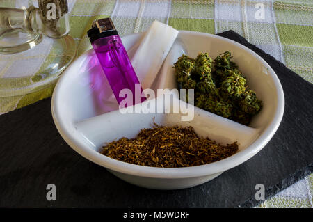 Big crystal bong and plate with materials to roll a joint and smoke. Nice presentation of buds of marijuana, tobacco, lighter and rolling paper. Stock Photo