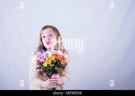 Twelve-year-old girl with long, dirty blonde hair holding colorful bouquet of daisies with look of admiration against white background Stock Photo
