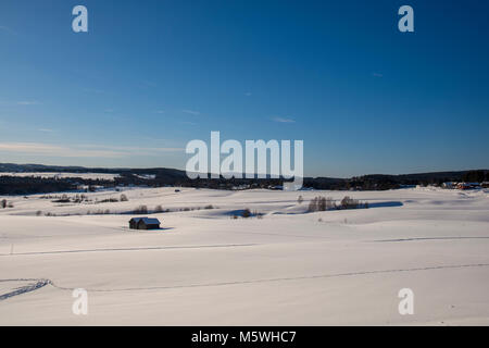 Snow covered field with some barns and a village in background , mountains and a blue sky in background , picture from Northern Sweden. Stock Photo