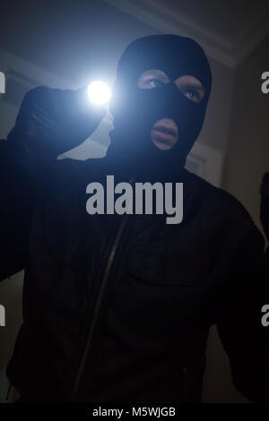 Thief wearing mask with a flashlight in the house. Stock Photo