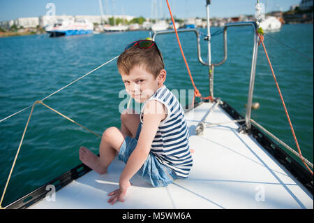 cute little boy in shorts and a striped t-shirt sits on Board the yacht in sea port Stock Photo