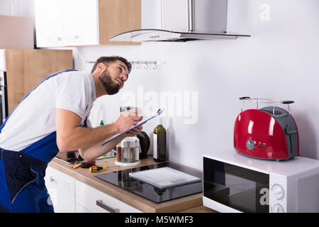 Young Male Technician Writing On Clipboard In Front Of Kitchen Extractor Filter Stock Photo