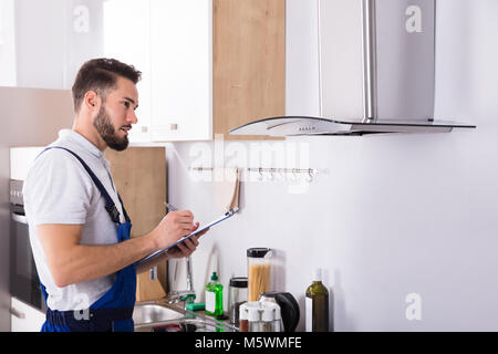 Young Male Technician Writing On Clipboard In Front Of Kitchen Extractor Filter Stock Photo