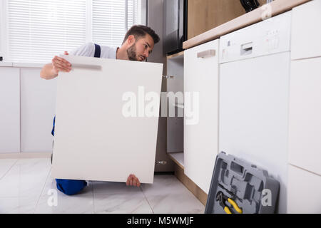 Young Handyman Fixing Sink Door In Kitchen Stock Photo