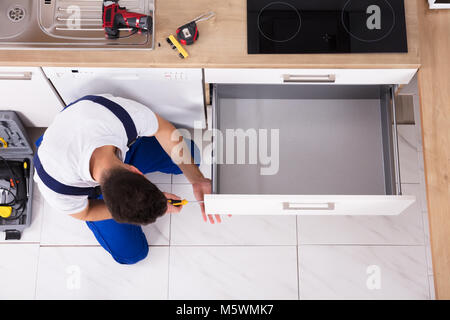 High Angle View Of Male Carpenter Fixing Drawer In Kitchen Stock Photo