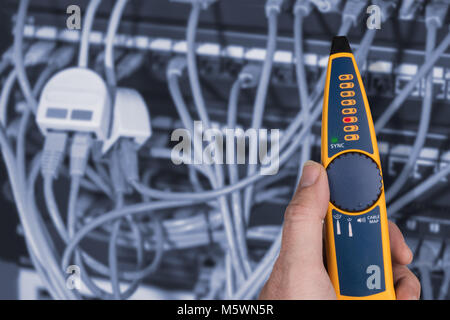 Measurement a cables connected in patch panels of rack case. Detail of expert's hand holding the probe to detect problems of structured cabling. Stock Photo