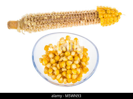 Yellow boiled corn and empty cob. Partly eaten corncob and pile of maize grains in glass bowl isolated on white background. Stock Photo
