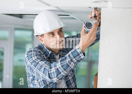 technician installing camera on wall using electric cordless drill Stock Photo