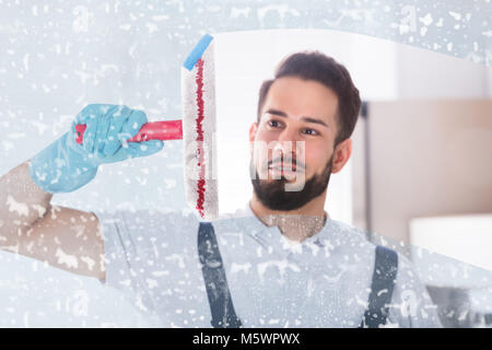 Young Male Janitor Cleaning Soap Sud On Window With Squeegee Stock Photo