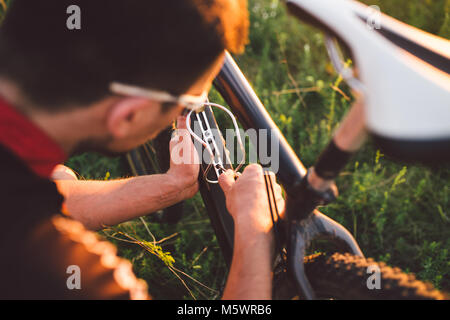 The guy sets the Bottle Cage on a mountain bike in a field on the nature at sunset of the day Stock Photo
