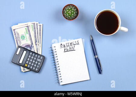 Notepad with pen, coffee, dollars, calculator and cactus on a blue background. Copy the space. Top view. Financial, marketing, business plan Stock Photo