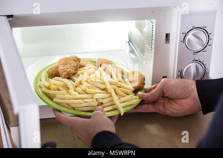 Close-up Of A Person's Hand Putting Fried Food Inside Microwave Oven Stock Photo