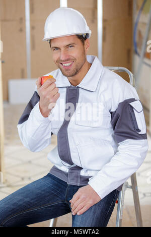 handsome young construction worker eating red apple on site Stock Photo