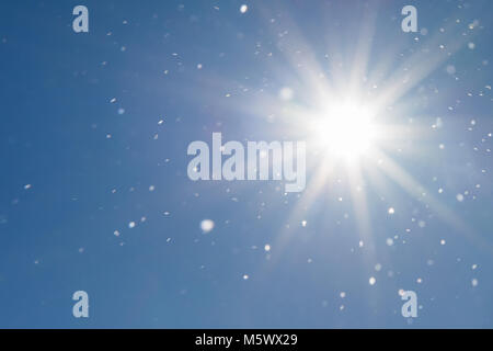 Background of cloudless blue sky and sunbeams illuminating snow flakes into the air Stock Photo