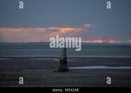 Snow arrived in the Southend Borough at dusk, as the sun set behind the Crowstone at Chalkwell, Essex, UK. Thames Estuary at low tide. PLA limit marker Stock Photo
