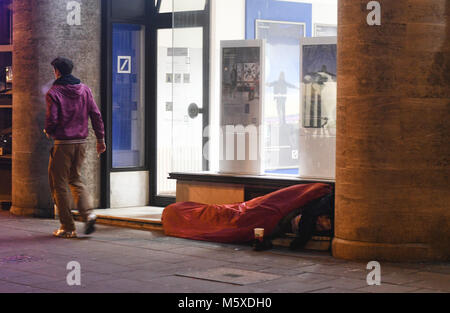 27 February 2018, Germany, Cologne: A homeless person sleeps in front of a bank at icy temperatures. Photo: Henning Kaiser/dpa Stock Photo