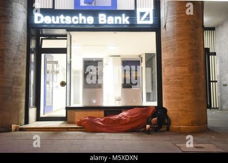 27 February 2018, Germany, Cologne: A homeless person sleeps in front of a bank at icy temperatures. Photo: Henning Kaiser/dpa Stock Photo