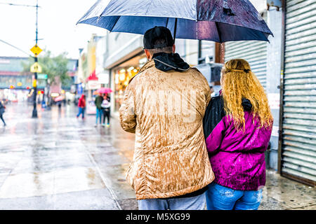 Bronx, USA - October 29, 2017: Road street in Fordham Heights center with stores, New York City, NYC during day, heavy rain, wet back couple walking u Stock Photo