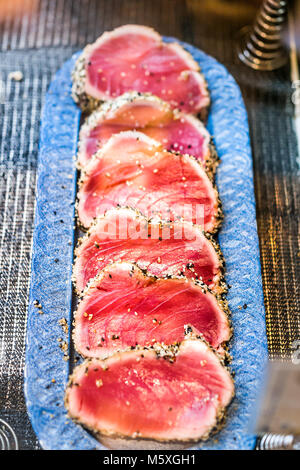Seared raw ahi tuna rare steaks with black pepper crust on display in market, restaurant, shop, deli counter, sesame seeds Stock Photo