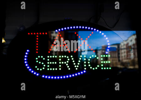 Closeup of neon tax service sign on door of public accountant colorful lights background with reflection of city building Stock Photo