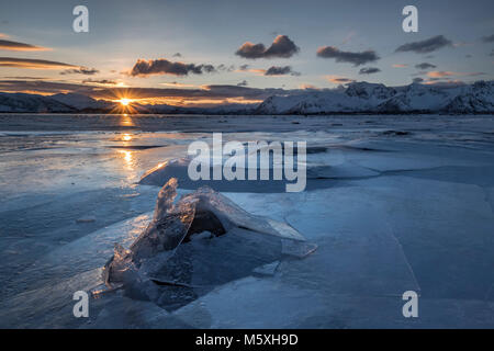 Broken ice, frozen fjord with mountains at sunset, solar reflex, Gimsoy, Lofoten, Norway Stock Photo