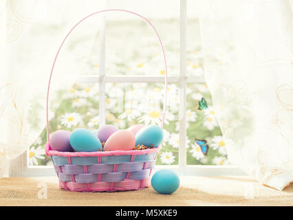 Easter shopping theme: colorful eggs in a basket on the window in a sunny day with butterflies Stock Photo