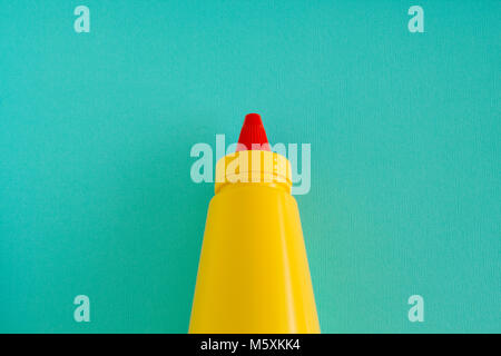 A bright yellow squirting mustard or condiment bottle with bright red twisting lid. Centre aligned on an aqua background. Stock Photo