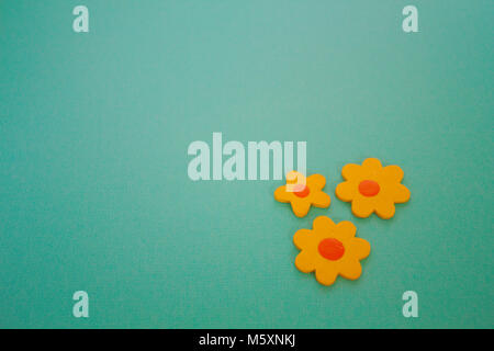 Three wooden  yellow craft flowers, two large & one small, with a bright orange centre. Bottom right aligned on an aqua background. Stock Photo