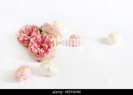 Spring greeting card, invitation. Pink and white Easter eggs with golden spots and rose flowers lying on white table. Feminine styled stock photo, floral composition. Stock Photo
