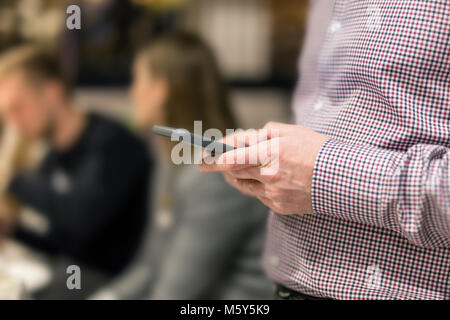 Man in shirt holding smartphone in hand.  Businesman using phone during corporate meeting Stock Photo