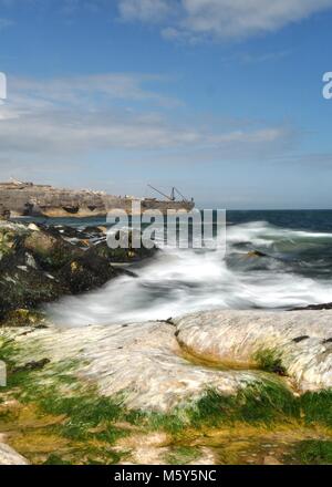 Sea landscape of the crane at Portland Bill in Dorset. Seaweed covered rocks in foreground with slow exposure waves and blue sky with clouds. Stock Photo