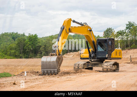 Yellow backhoe excavating soil and sand to construct water reservoir. Stock Photo