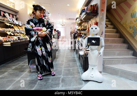 A Japanese woman dressed in Kimono interacting with a robot. Stock Photo