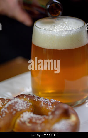 pouring beer into a large glass mug on plate with warm soft pretzel appetizer Stock Photo