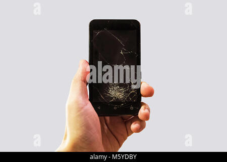A man holding a black phone with a black broken glass on the screen. Cracked smartphone in hand holding. Stock Photo