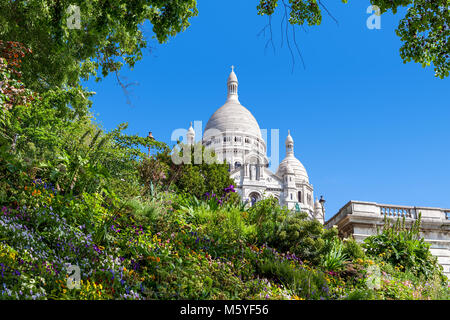 Green flowerbed with flowers as famous Sacre-Coeur Basilica on background under blue sky in Paris, France.