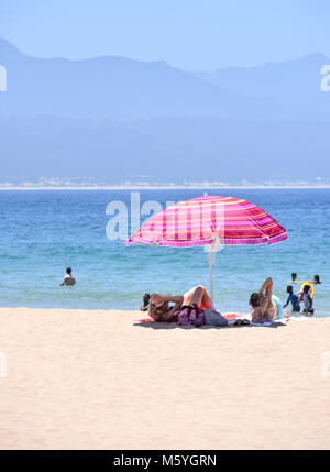 On the beach of Robberg near Plettenberg Bay in South Africa with Indian Ocean in the background and a colorful umbrella with tourists relaxing in the Stock Photo