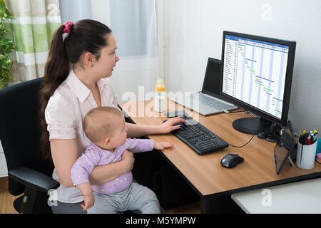 Mid Adult Woman With Baby Girl Looking At Gantt Chart On Computer Stock Photo