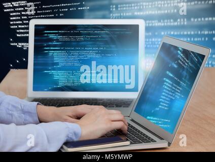Hands typing coding text on two laptops Stock Photo