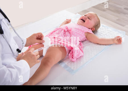 Doctor Giving Vaccine Injection To Crying Baby Girl In Clinic Stock Photo