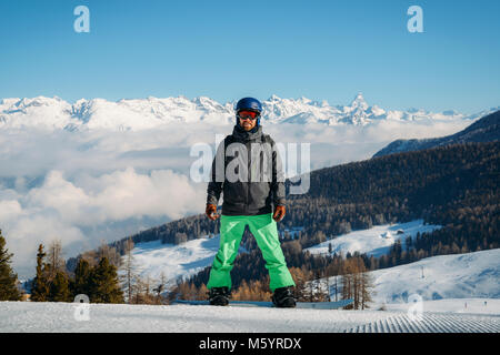 Full length shot of a smiling snowboarder standing on the slope in the mountains, looking to the camera at winter scene in Aosta, Italy Stock Photo