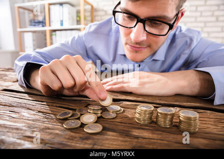Close-up Of A Young Businessman Counting Coins Over Wooden Desk Stock Photo