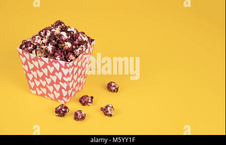 Pink popcorn with berry taste in paper cup on yellow background. Stock Photo