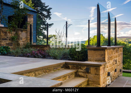 Corner of beautiful, landscaped, private garden (contemporary design, paved path, steps, glass screen, border shrubs, plants) Yorkshire, England, UK Stock Photo