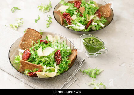 Two bowls with frisee lettuce salad, sun dried tomatoes, cheese, bread chips and pesto dressing Stock Photo